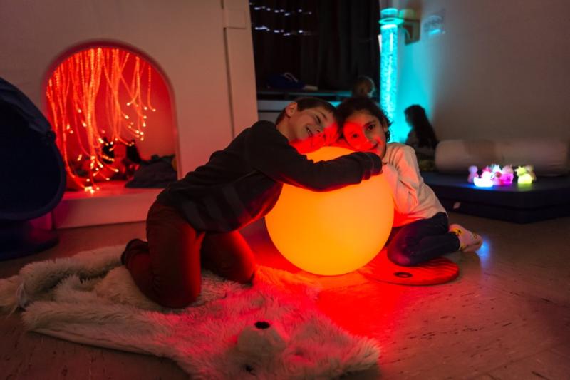 Jongen en meisje knuffelen lichtlamp in snoezelruimte van Leerexpert De IJsduiker